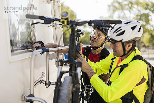 Friends wearing helmet and adjusting bicycle behind van