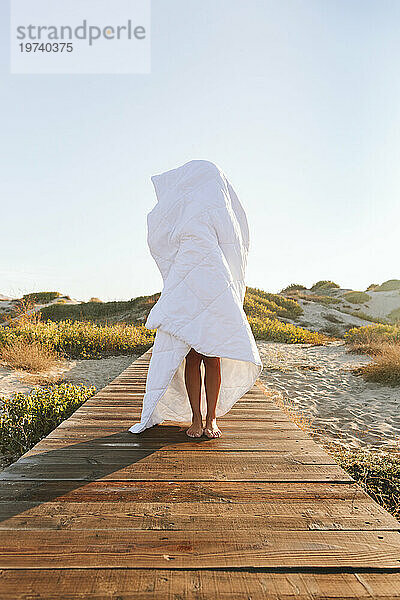 In eine Decke gehüllte Frau steht auf der Promenade am Strand