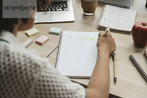 Teenage girl making notes on notepad at desk