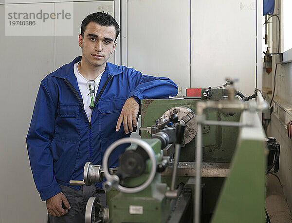 Confident trainee leaning on lathe at workshop