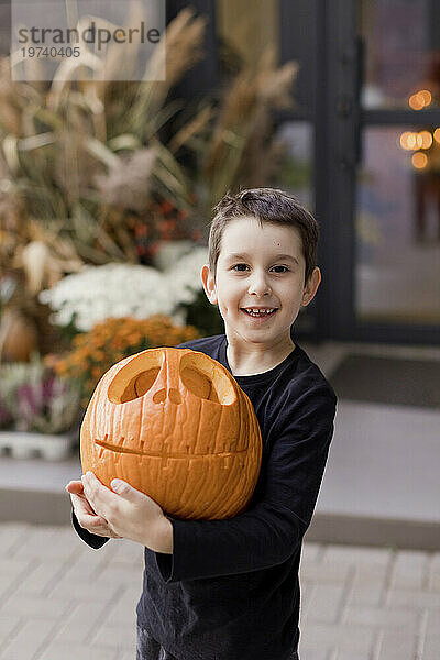 Smiling boy holding carved pumpkin in hand