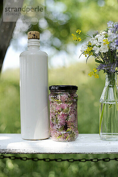 White bottle  jar of chive flowers and blooming bouquet on bench