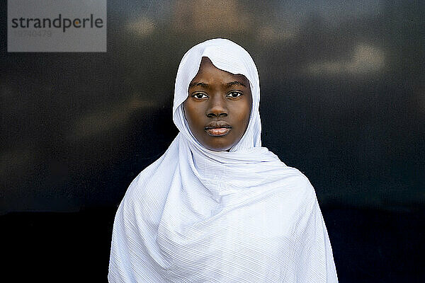 Ernsthafte junge Frau mit Hijab vor schwarzer Wand