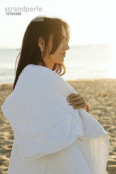 In eine Decke gehüllte Frau steht am Strand
