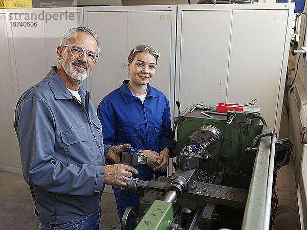 Lächelnder Auszubildender steht mit Ausbilder in der Nähe der Drehmaschine in der Werkstatt