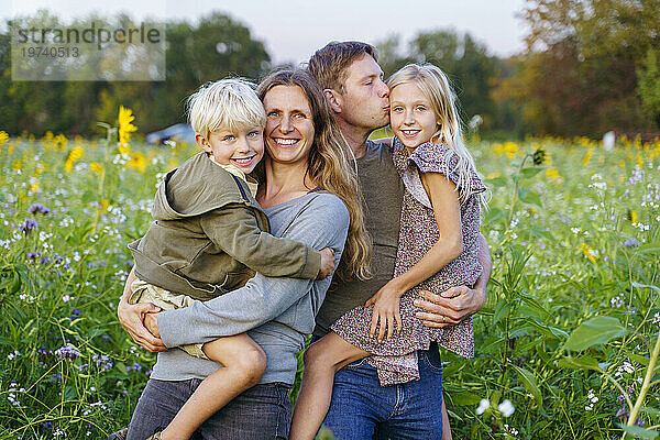 Glückliche Eltern  die Kinder im Sonnenblumenfeld tragen