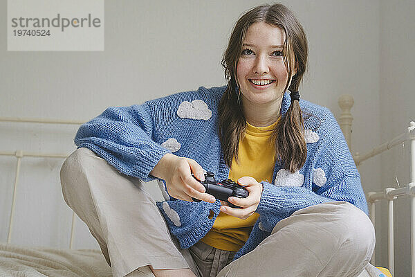 Happy teenage girl playing video game with controller on bed