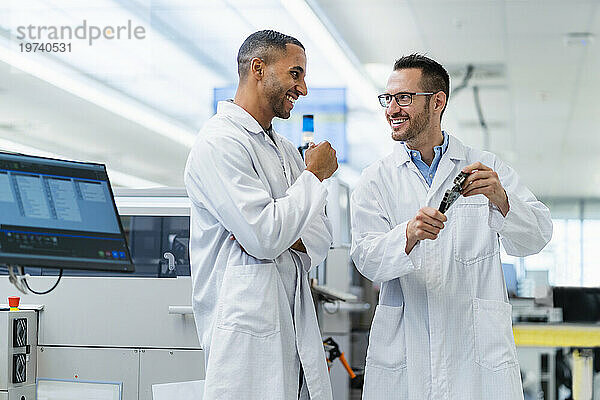Zwei lächelnde Kollegen in der Elektronikfabrik treffen sich mit Motherboard