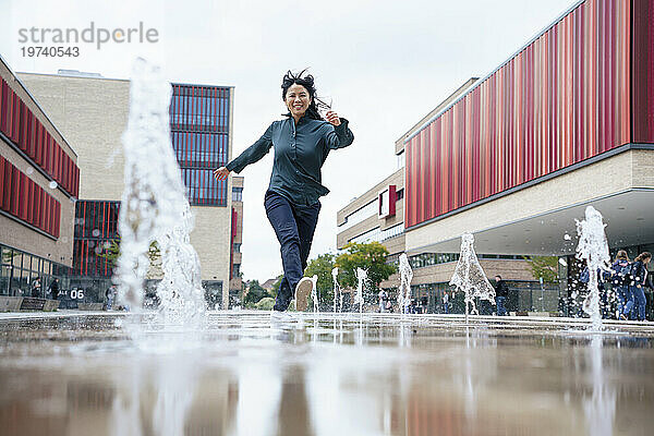 Fröhliche Geschäftsfrau läuft in der Nähe von Wasserfontänen im Büropark