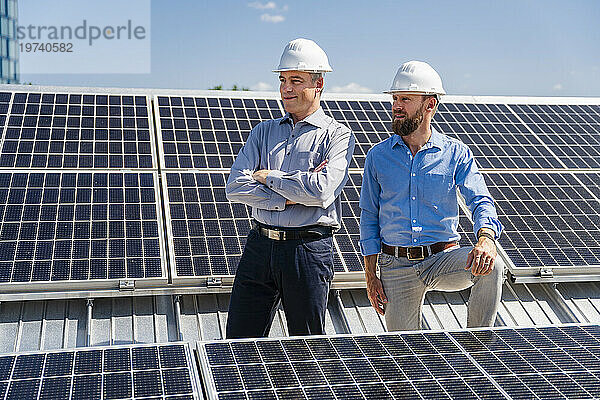 Zwei Geschäftsleute mit Schutzhelmen strahlen Selbstvertrauen aus  während sie inmitten eines Feldes aus Solarpaneelen stehen