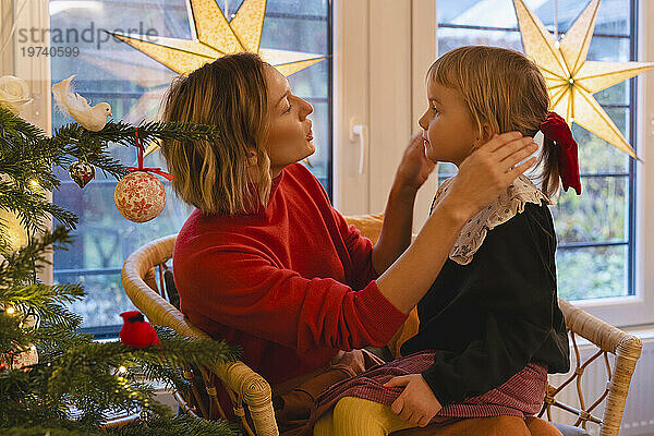 Mutter spricht mit Mädchen und passt ihr Haar am heimischen Weihnachtsbaum an