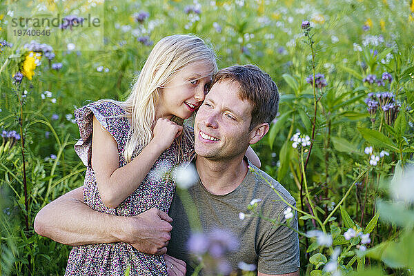 Smiling daughter whispering to father in field