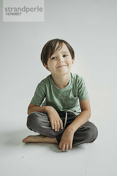 Lächelnder Junge sitzt vor weißem Hintergrund