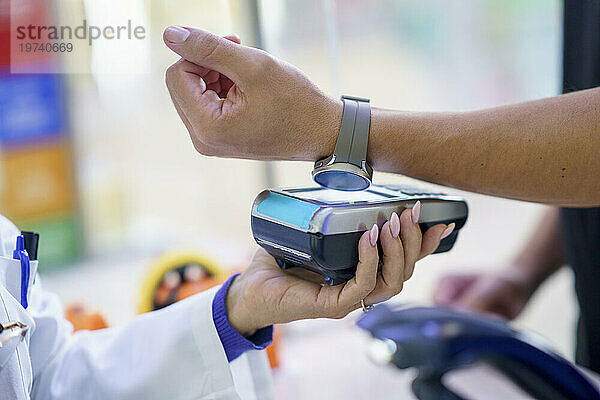 Hand of customer paying via tap to pay method through smart watch at pharmacy