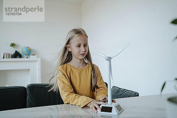 Blondes Mädchen spielt zu Hause mit Windkraftanlage auf dem Tisch