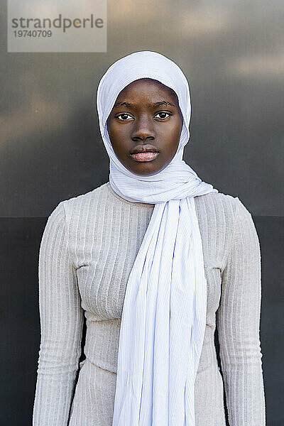 Ernsthafte junge Frau mit Hijab vor der Wand