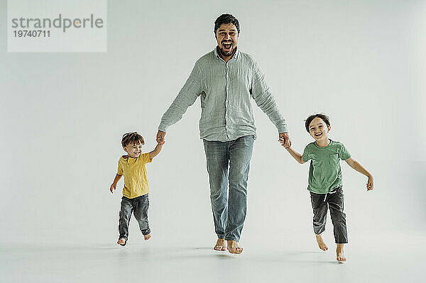 Happy father holding hands with children and running against white background