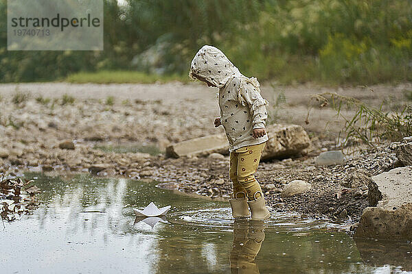Girl with paper boat floating on water puddle