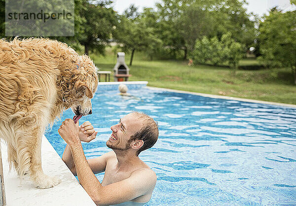 Glücklicher Mann streichelt Golden Retriever Hund und genießt es im Schwimmbad