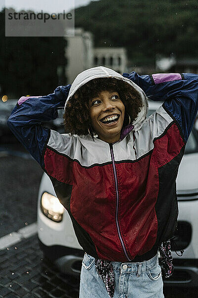 Glückliche junge Frau trägt Kapuzenjacke im Regen