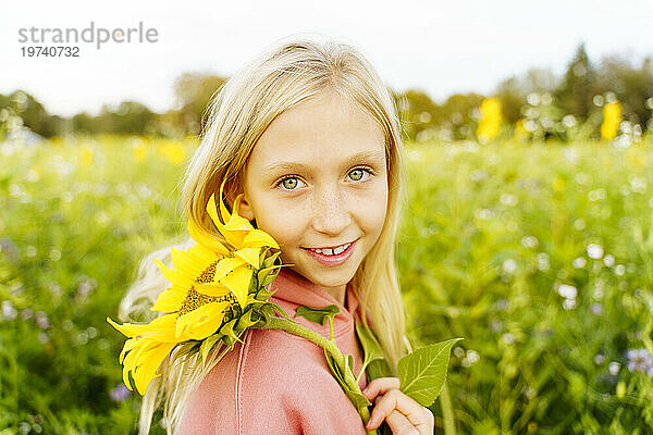 Lächelndes blondes Mädchen hält Sonnenblume im Feld