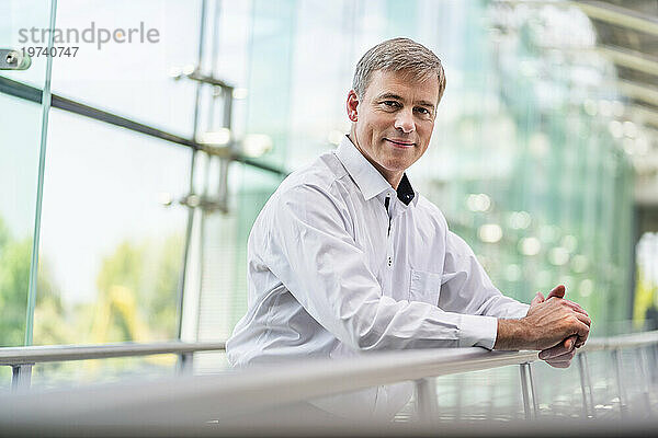 Confident businessman leaning on railing in office building