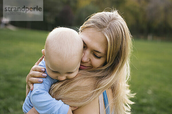 Liebevolle Mutter trägt und umarmt Sohn im Park