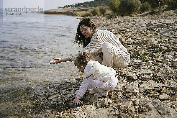 Glückliche Mutter spielt mit Tochter am See