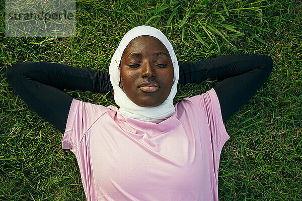 Junge Frau mit den Händen hinter dem Kopf im Gras liegend