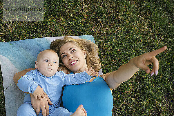 Happy mother gesturing and lying with son on exercise mat at park
