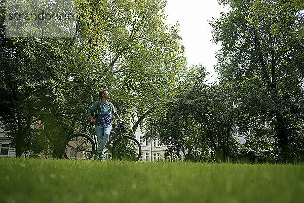 Mann stützt sich auf Fahrrad und blickt auf Bäume im Park