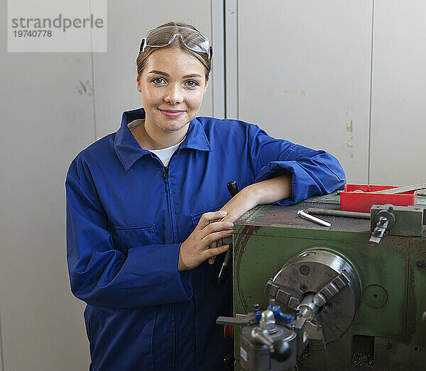 Smiling apprentice leaning on lathe at workshop