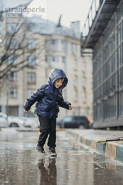 Netter Junge  der nach Regen auf nasser Straße spielt