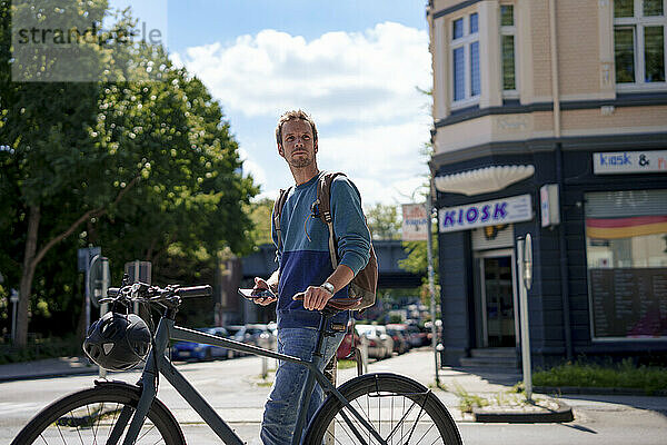 Reifer Mann hält Smartphone in der Hand und steht an einem sonnigen Tag mit dem Fahrrad