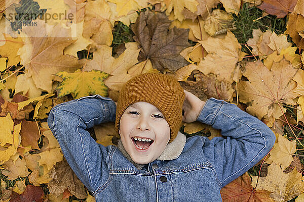 Fröhlicher Junge liegt auf gelben Ahornblättern im Herbstpark