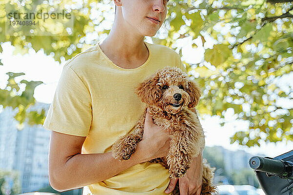 Junger Mann im gelben T-Shirt hält Hund unter Baum