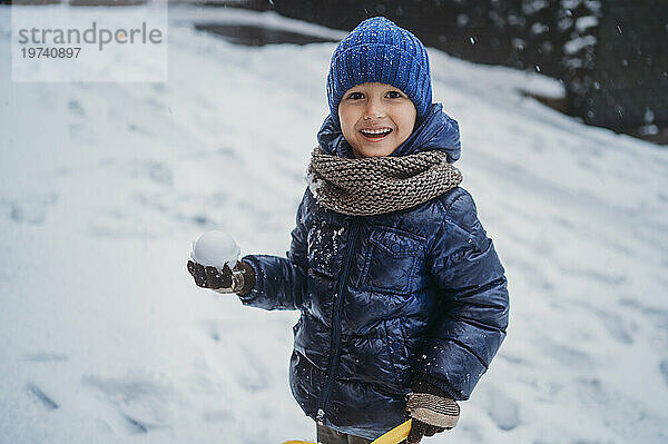 Fröhlicher Junge hält Schneeball im Winter