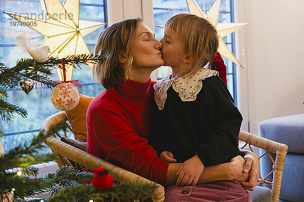 Nettes Mädchen küsst Mutter in der Nähe des Weihnachtsbaums im Haus