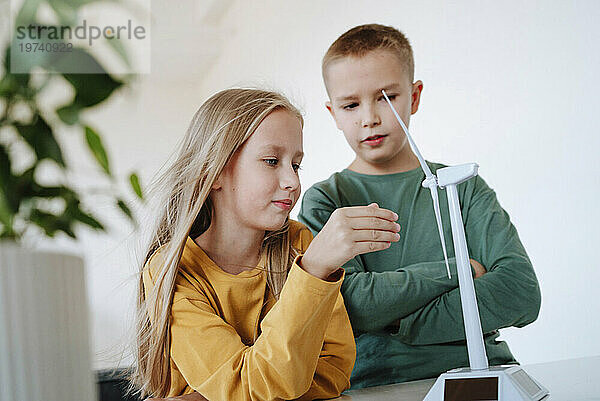 Blonder Bruder und Schwester untersuchen zu Hause das Modell einer Windkraftanlage