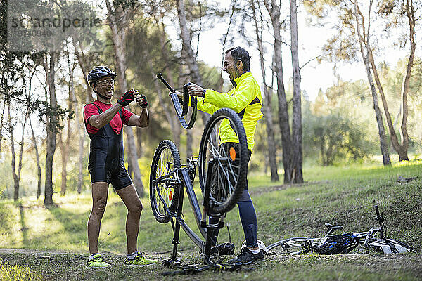 Lächelnde Freunde reparieren Fahrrad im Wald