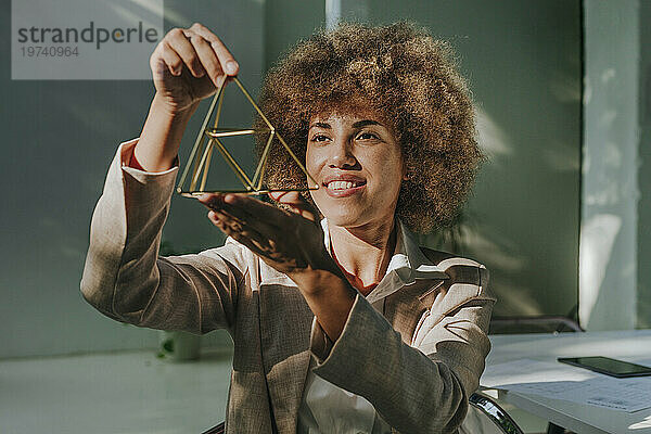 Glückliche Geschäftsfrau untersucht Metallpyramide im Büro