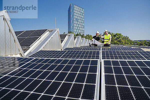 Zwei Techniker planen auf dem Dach eines mit Solarpaneelen ausgestatteten Firmengebäudes