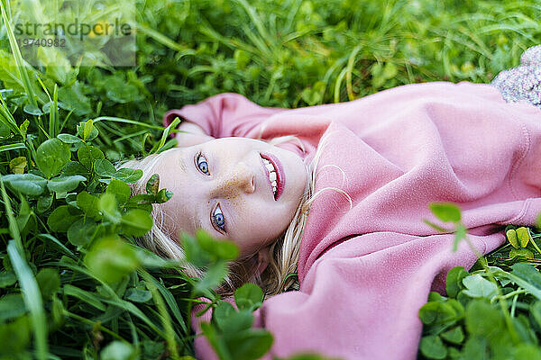 Lächelndes Mädchen in rosafarbenem Sweatshirt  das auf Gras liegt