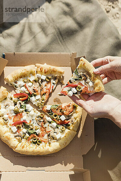 Hände einer Frau  die an einem sonnigen Tag ein Pizzastück hält