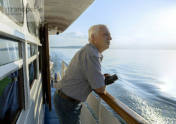 Älterer Mann mit Fernglas in der Hand  der an einem sonnigen Tag vom Schiff aus auf das Meer blickt