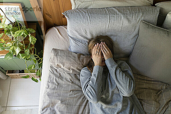 Gestresste Frau mit Händen  die ihr Gesicht bedecken  liegt zu Hause im Bett