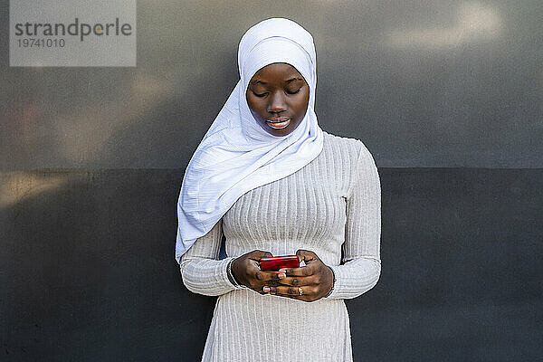 Junge Frau mit Hijab benutzt Smartphone vor der Wand
