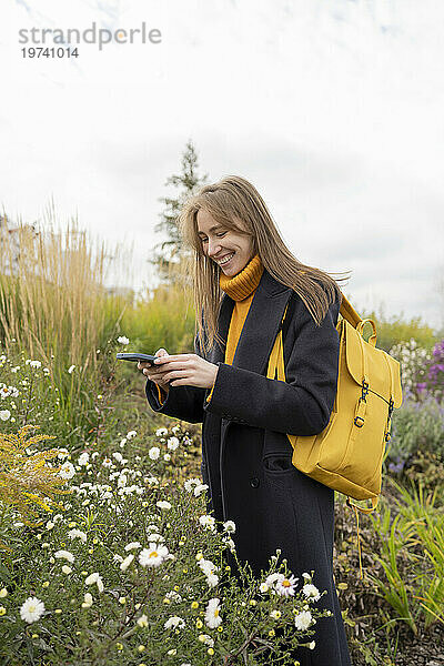 Glückliche Frau fotografiert Blumen per Smartphone im Park