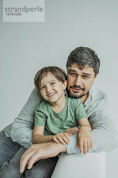 Lächelnder Mann mit Sohn sitzt auf Sofa vor weißem Hintergrund