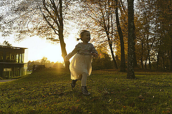 Glückliches Mädchen  das bei Sonnenuntergang in der Nähe eines Baumes im Park rennt